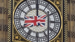 A British Union flag flutters in front of one of the clock faces of the 'Big Ben' clocktower of The Houses of Parliament in central London