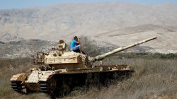 A man sits on an old tank as he watches fighting taking place in Syria as seen from the Israeli side of the border fence between Syria and the Israeli-occupied Golan