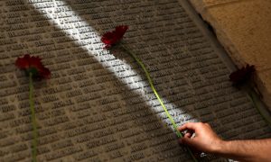 A man lays a flower on a monument engraved with names of victims of the September 11th attacks, during a memorial event marking the 15th anniversary