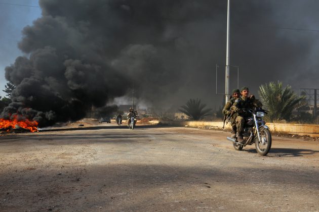 Rebel fighters drive their motorcycles under the smoke of burning tyres, western Aleppo city,