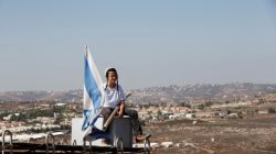 A boy sits near an Israeli flag atop the roof of a vehicle at the entrance to the Jewish settler outpost of Amona in the West Bank