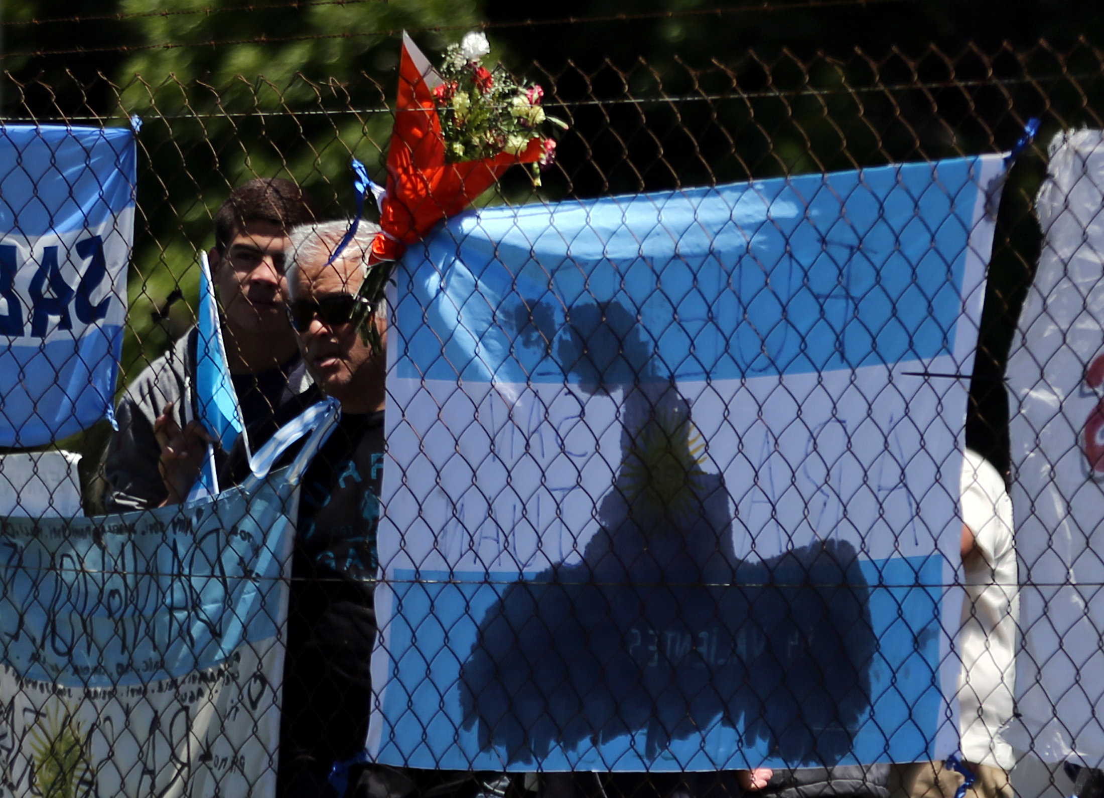 People stand next to a bouquet of flowers and banners in support of the 44 crew members of the missing at sea ARA San Juan submarine, outside an Argentine naval base in Mar del Plata, Argentina November 25, 2017.