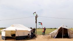 A man hangs a Palestinian flag at an electric pole near the border with Israel, in the southern Gaza Strip March 28, 2018. REUTERS/Ibraheem Abu Mustafa
