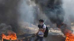 A Palestinian passes burning tires during clashes with Israeli troops at a protest demanding the right to return to their homeland, at the Israel-Gaza border east of Gaza City April 6, 2018. REUTERS/Mohammed Salem