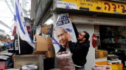 A man holds a Likud election campaign poster depicting Israeli Prime Minister Benjamin Netanyahu as he stands behind a stall at Mahane Yehuda Market in Jerusalem April 8, 2019. REUTERS/Ronen Zvulun