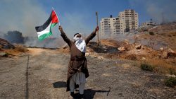 FILE PHOTO: A demonstrator holds a Palestinian flag and a cane during a protest against the Israeli demolitions of Palestinian homes in the village of Sur Baher which sits on either side of the Israeli barrier in East Jerusalem and the Israeli-occupied West Bank July 26, 2019. REUTERS/Mussa Qawasma